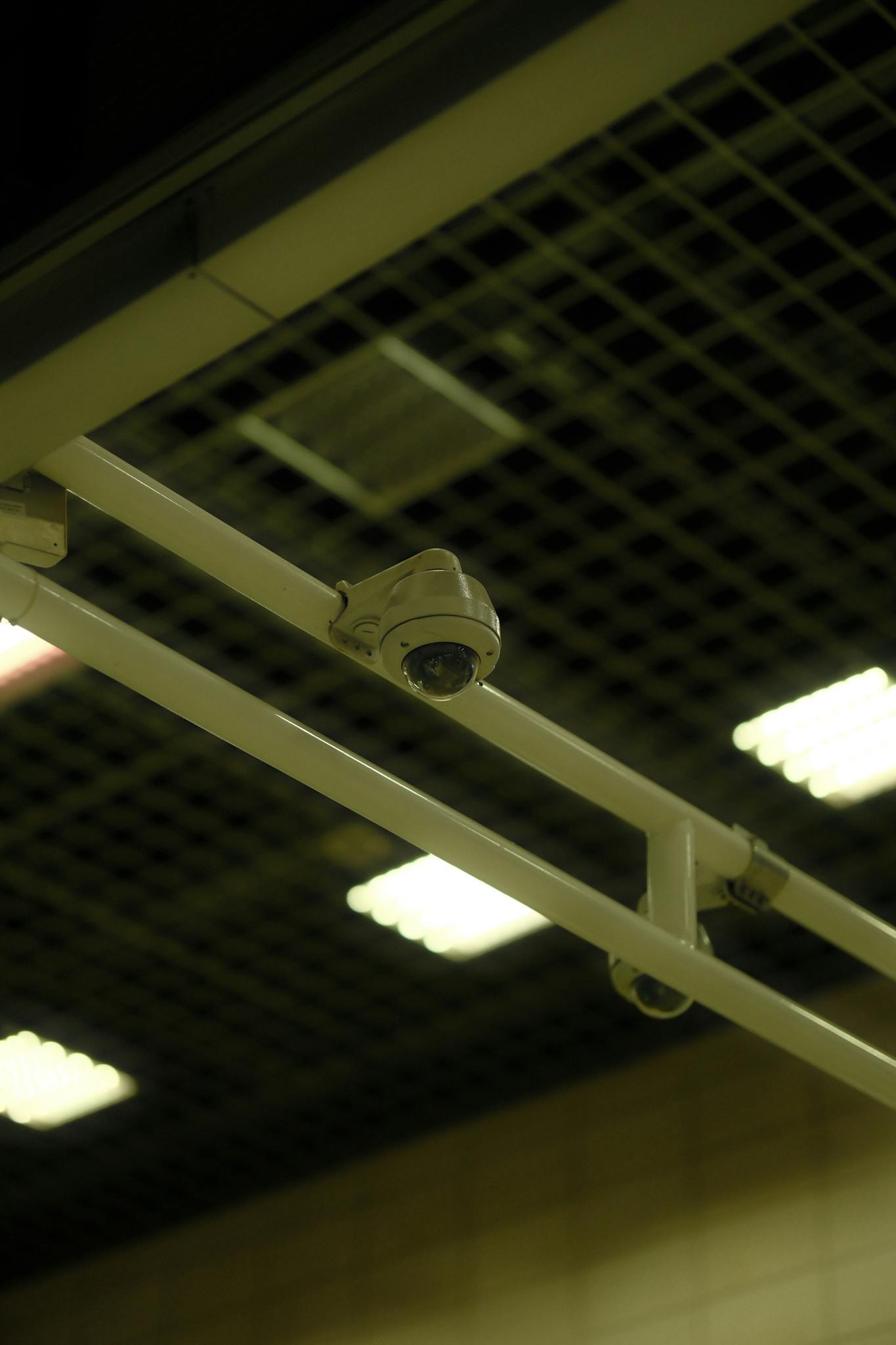 Close-up of a ceiling-mounted security camera in an indoor environment with grid and lights.