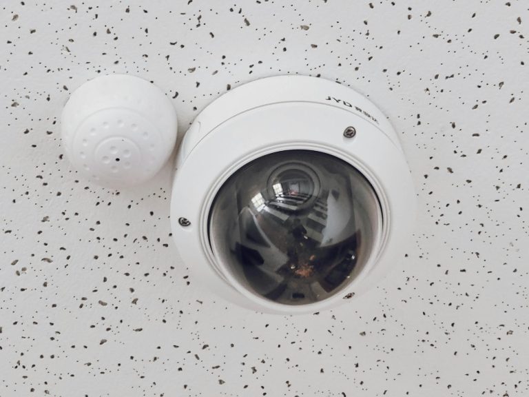 Close-up of a round dome surveillance camera installed on a speckled ceiling for security monitoring.