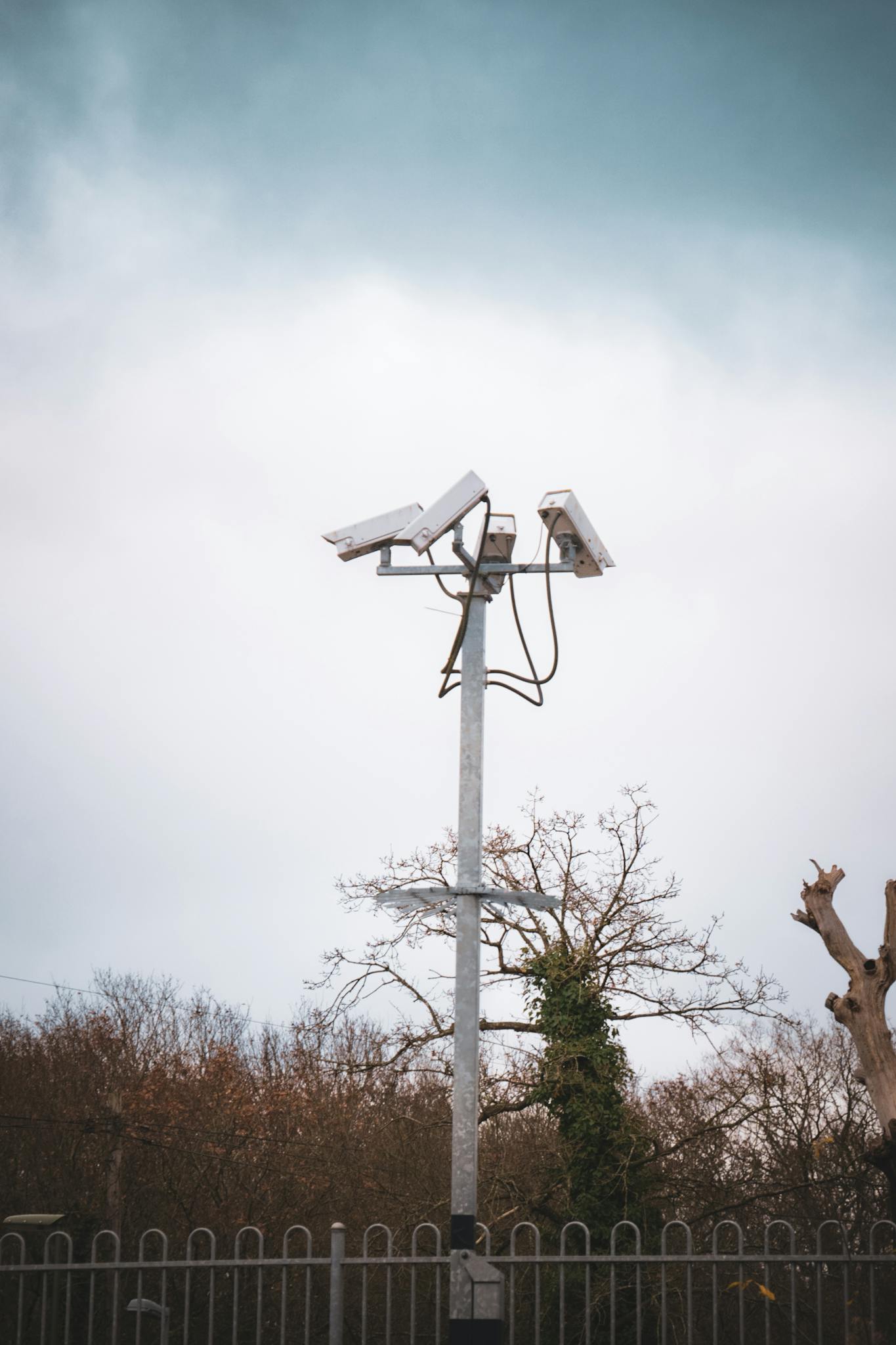 Outdoor security cameras mounted on a tall metal pole against a cloudy sky, ensuring surveillance.